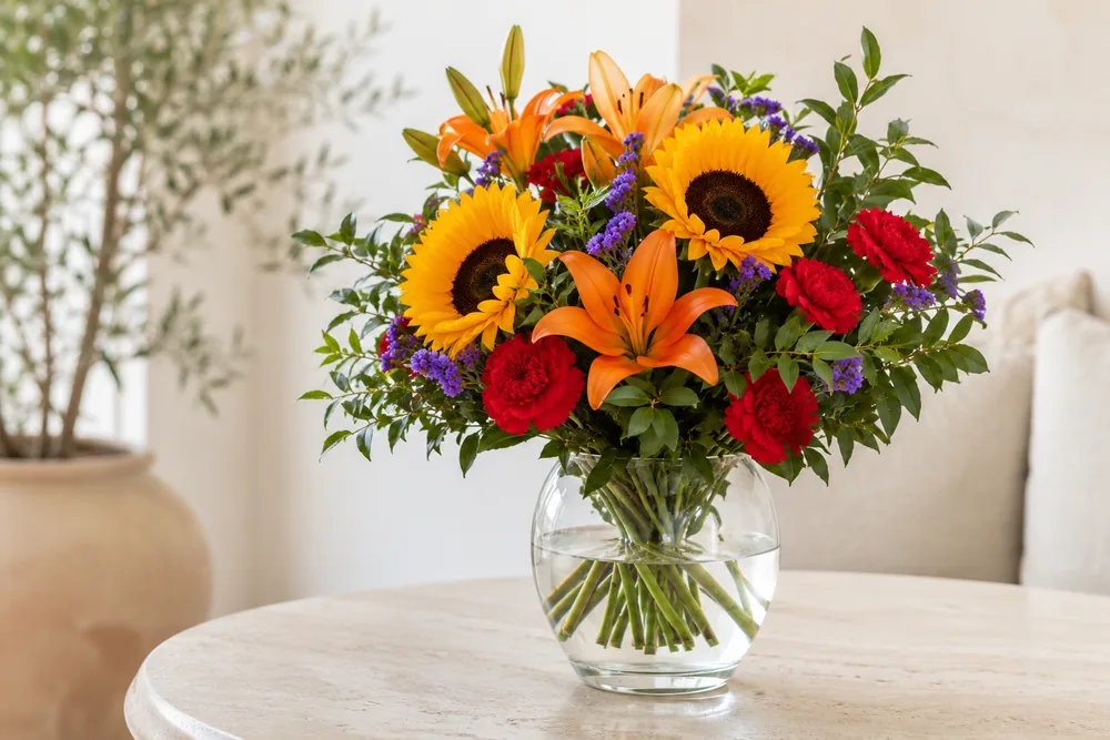 Ramo de girasoles, lilium y claveles en un jarrón con agua limpia