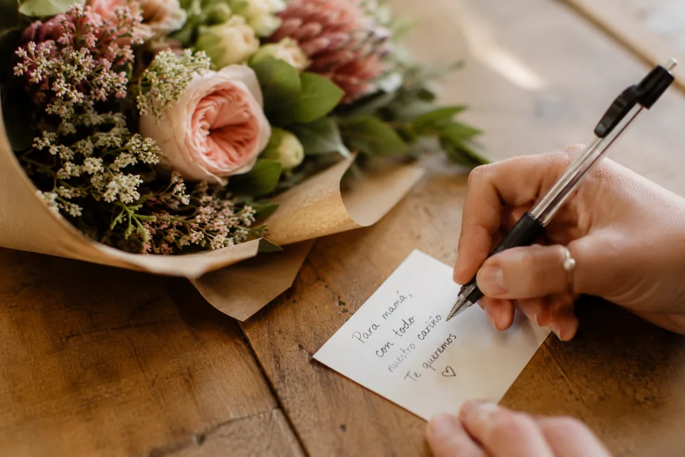 Mano escribiendo una dedicatoria junto a un ramo de flores