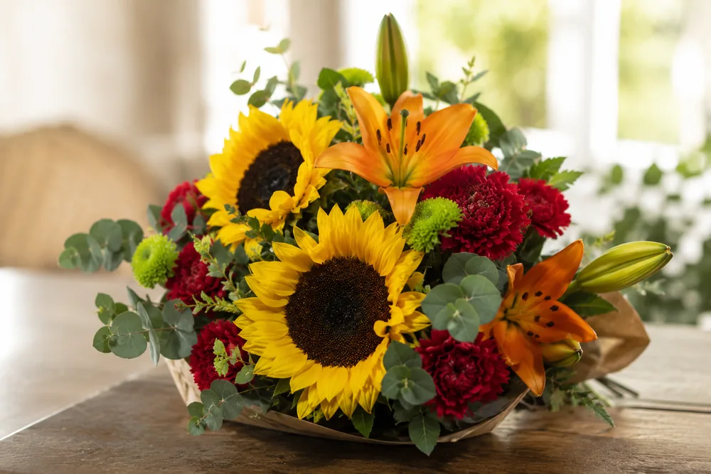 Ramo de verano con girasoles, lilium y claveles sobre una mesa luminosa